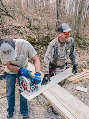 construction volunteer cutting wood with saw staff member holding board at Deer Run Camps & Retreats