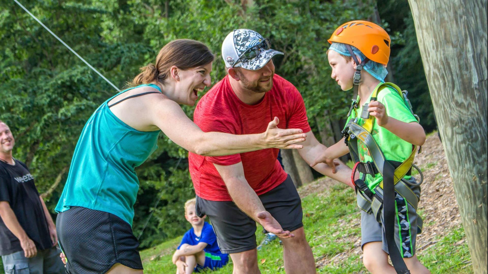 family camper parents and son in harness with orange helmet at giant swing at Deer Run Camps & Retreats