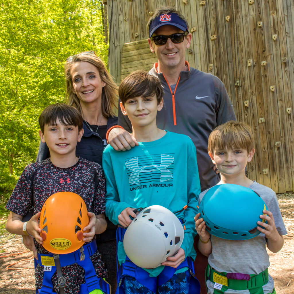 parents with 3 boys at family camp standing with harness and helmets at the climbing wall at Deer Run Camps & Retreats