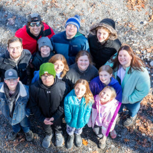 Overnight Winter Campers looking up at the camera, smiling brightly from the bottom of the Aerial Quest High Ropes course at Deer Run Camps & Retreats.