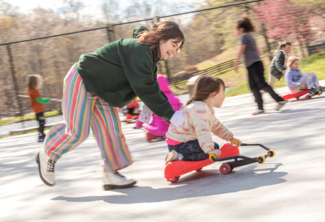 A camp counselor pushes her Spring Break Camper on a roller Racer and both smile brightly at Deer Run Camps and Retreats.