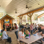 Deer Run Camps Open house event taking place- guests socialize at creekside veranda as staff greet and tell them about Summer Camps.