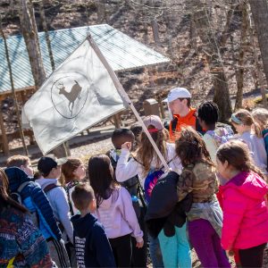 A group of winter day campers gather around their group flag displaying the Deer Run Logo at Deer Run Camps & Retreats Winter Day Camp.