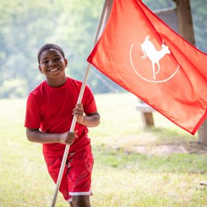 Boy daycamper holding his group flag displaying Deer Run Camps & Retreats Logo. (Square crop)