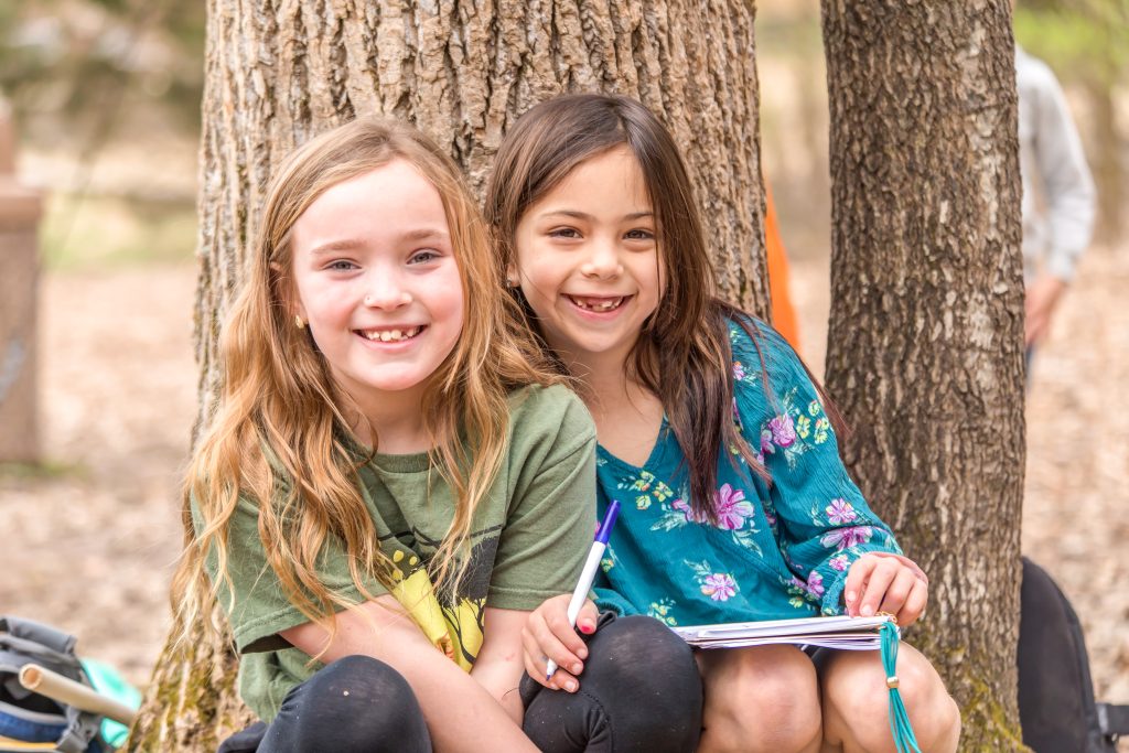 Two girl winter day campers smile for a photo by a tree at Deer Run Camps & Retreats.